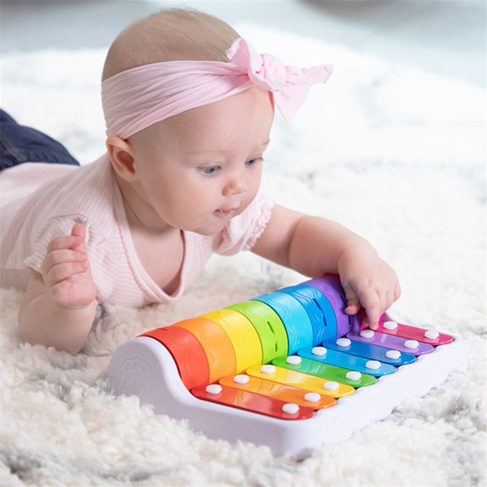 Baby hands playing a colorful roller piano toy with rainbow keys