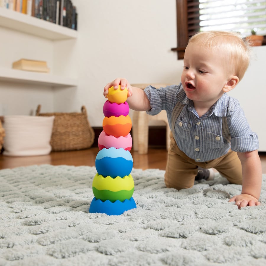 Child playing with Neo tactile stacking tower with five scalloped, bright pieces