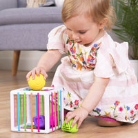 Baby playing with a white shape-sorting toy cube and colorful pieces