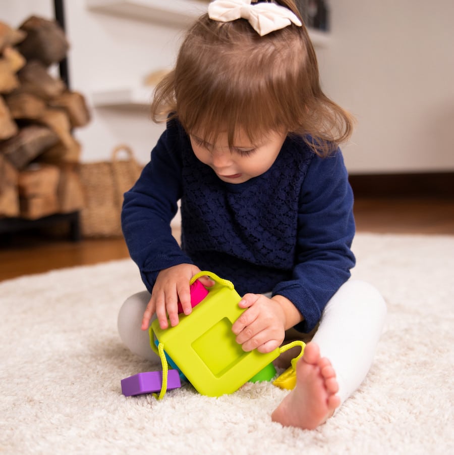 Lime and purple shape-sorting cube toy with rope handles and square openings