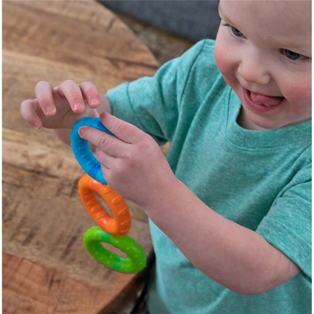 Child holding bright stacking rings toy: blue, orange, and green circular rings.