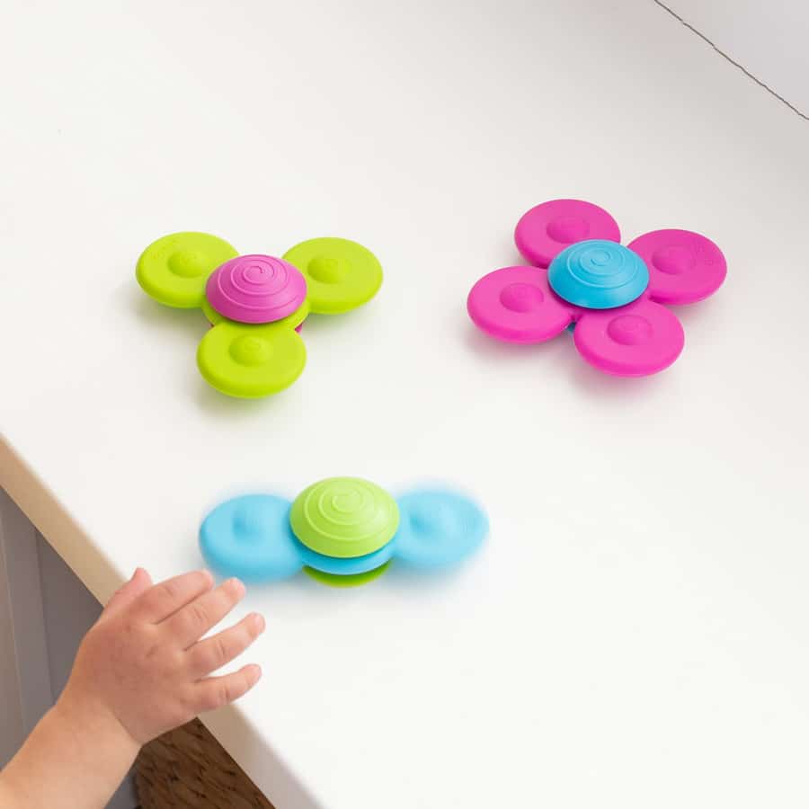 Three flower-shaped spinner discs in lime green, pink, and blue on a white floor