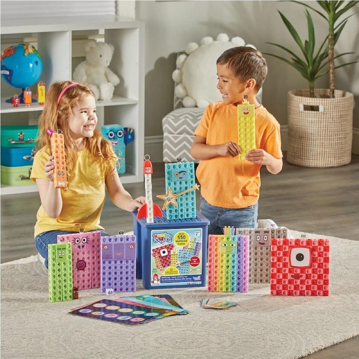 Two children holding Numberblocks-style cube characters near an open cube storage case